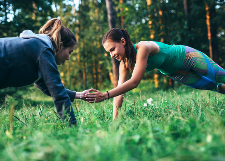 Två kvinnor tränar och gör plankan i naturen
